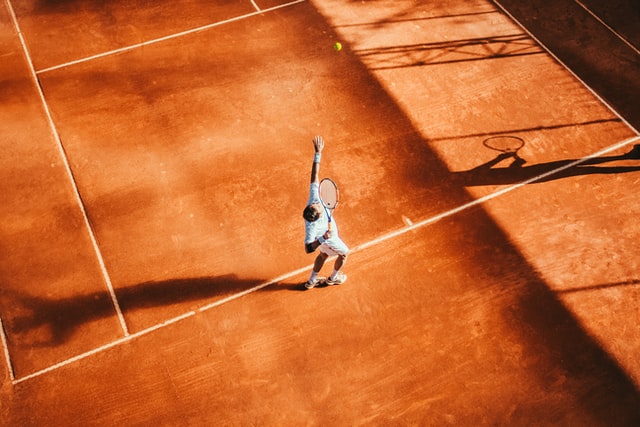 man serving on a clay tennis court in Mouratoglou Tennis Academy